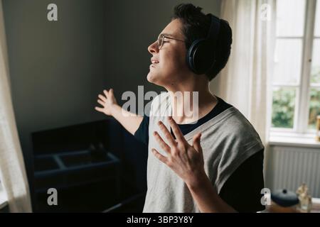 Junger Mann singt und tanzt, während er Musik über kabellose Kopfhörer zu Hause hört Stockfoto