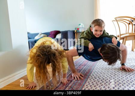 Vater macht Liegestütze mit Sohn und Tochter auf Teppich im Wohnzimmer zu Hause Stockfoto