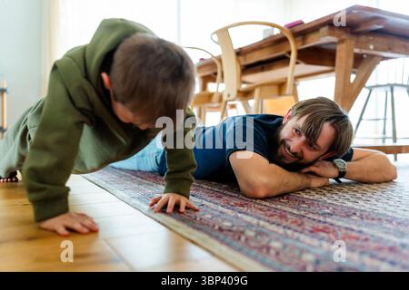Lächelnder Vater, der den Sohn ansieht, der Liegestütze im Wohnzimmer zu Hause macht Stockfoto