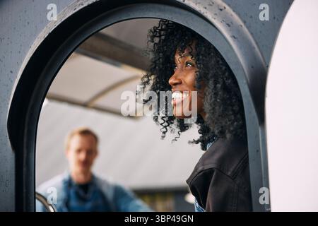 Lächelnde reife Frau mit lockigem Haar, die durch das Fenster des Food Trucks nach draußen blickt Stockfoto