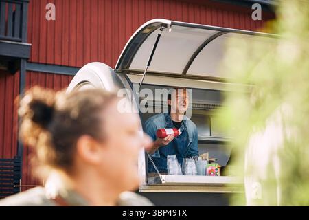 Niedriger Blickwinkel eines glücklichen Mannes, der Ketchup-Flasche hält, während er im Food Truck arbeitet Stockfoto