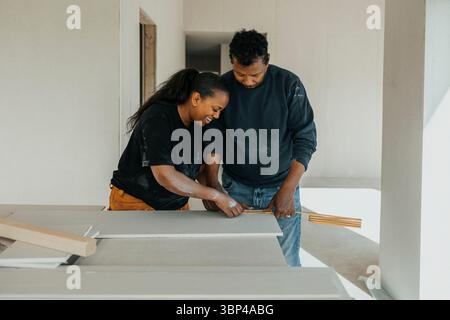 Männlicher Arbeiter hilft weiblichen Kollegen bei der Messung von Holzdielen mit Bandmaß beim Hausbau Stockfoto