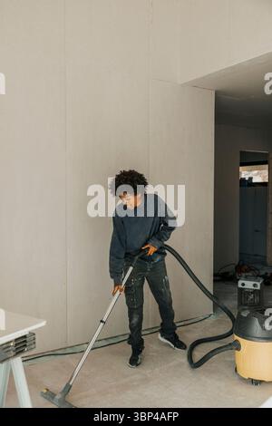 Boy, der den Boden mit Staubsauger auf der Baustelle reinigt Stockfoto
