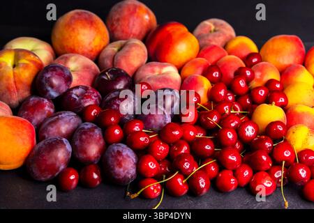 Pfirsiche, Pflaumen und Kirschen auf einer dunklen Oberfläche angeordnet Stockfoto