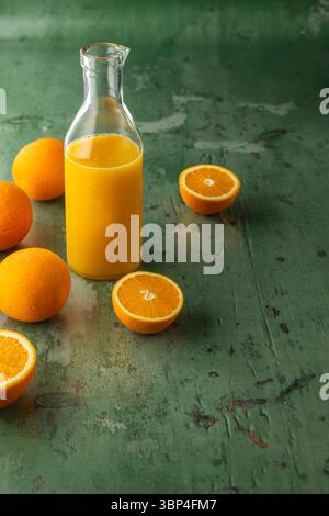 Glasflasche mit frischem Orangensaft und geschnittenen Orangen auf grüner Oberfläche Stockfoto