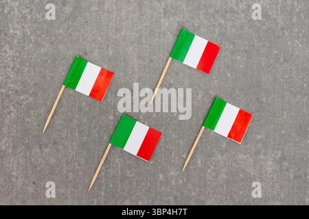 Vier italienische Miniflaggen diagonal auf grauem Hintergrund angeordnet Stockfoto