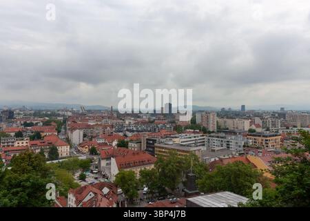 Ein weitläufiger Blick auf die Höhe fängt das Stadtbild von Ljubljana, Slowenien, an einem bewölkten Tag ein. Rot gekachelte Dächer dominieren den Vordergrund und zeigen die Stockfoto