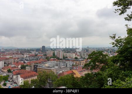 Ein weitläufiger Blick auf die Höhe fängt das Stadtbild von Ljubljana, Slowenien, an einem bewölkten Tag ein. Rot gekachelte Dächer dominieren den Vordergrund und zeigen die Stockfoto