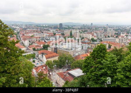 Ein weitläufiger Blick auf die Höhe fängt das Stadtbild von Ljubljana, Slowenien, an einem bewölkten Tag ein. Rot gekachelte Dächer dominieren den Vordergrund und zeigen die Stockfoto