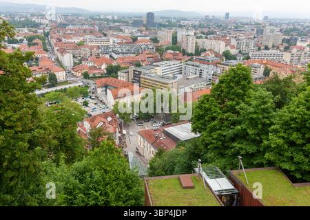 Ein weitläufiger Blick auf die Höhe fängt das Stadtbild von Ljubljana, Slowenien, an einem bewölkten Tag ein. Rot gekachelte Dächer dominieren den Vordergrund und zeigen die Stockfoto