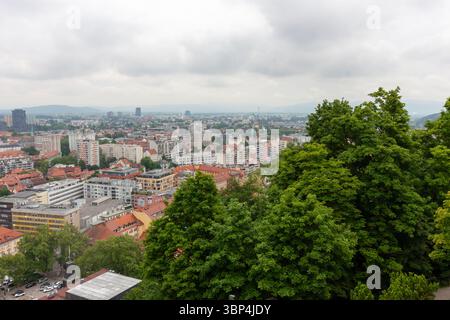 Ein weitläufiger Blick auf die Höhe fängt das Stadtbild von Ljubljana, Slowenien, an einem bewölkten Tag ein. Rot gekachelte Dächer dominieren den Vordergrund und zeigen die Stockfoto