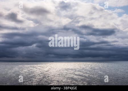 Stürmische Wolken sammeln sich über der Nordsee in der Nähe von Dänemark, von einem Kreuzfahrtschiff aus gesehen. Das silberne Wasser reflektiert Licht durch Brüche am dunklen Himmel. Stockfoto