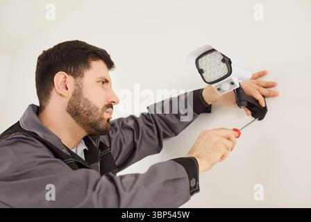 Professioneller Handwerker mit Schraubendreher zum Einrichten der Sicherheitskamera an der weißen Wand Stockfoto