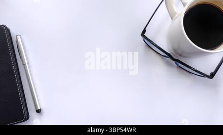 Minimalistischer, flacher Arbeitsbereich mit Stift, Notebook, Brille und einer Tasse Kaffee auf weiß. Ideal für Unternehmen, Planung, Produktivität und Zeitmanagement Stockfoto