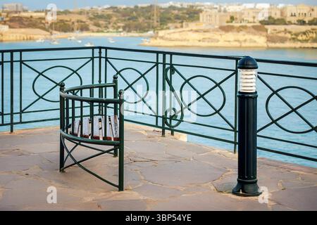 Meerblick mit geschwungener Metallbank mit Holzlatten auf der Steinterrasse neben schwarzer schmiedeeiserner Lampe und Geländer mit Blick auf die malerische Bucht Stockfoto