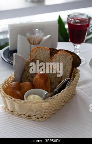 Brot im Korb. Weiß-schwarz geschnittenes Brot, Butter und Kuchen in einem Korb auf dem Tisch im Restaurant Stockfoto