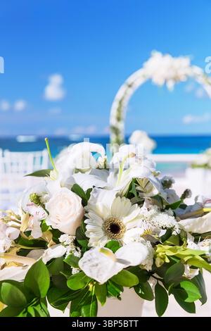 Blumenstrauß in einer Vase für die Hochzeitszeremonie und wunderschöner Hochzeitsbogen an einem tropischen Strand Stockfoto