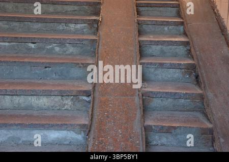 Alte Steintreppe mit Granitrampen für Kinderwagen, abgenutzt und verwittert. Zement zeigt Anzeichen von Alter und Zerfall, was auf eine langsame Verschlechterung im Laufe der Zeit hindeutet Stockfoto