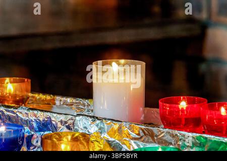 Farbenfrohe Votivkerzen, die in einer Kirche brennen, symbolisieren Gebet, Hoffnung und Hingabe in einer friedlichen religiösen Umgebung. Stockfoto