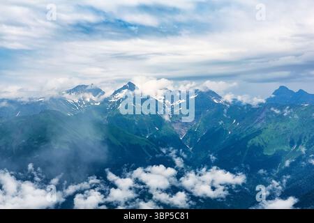 Neblige Berggipfel. Graue niedrige Wolken auf dem Gipfel des Berges. Gipfel von hohen Felsen mit Schnee in niedrigen Wolken. Stockfoto
