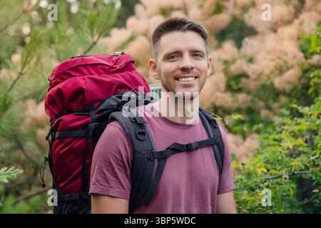 Glücklicher Rucksacktouristen, der während der Sommerwanderung im Wald lächelt. Outdoor-Reisen, Abenteuer und aktives Lifestyle-Konzept. Stockfoto