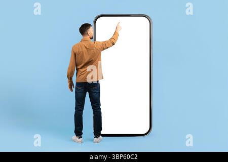 Rückansicht eines jungen Mannes, der auf den riesigen Smartphone-Bildschirm zeigt. Stockfoto