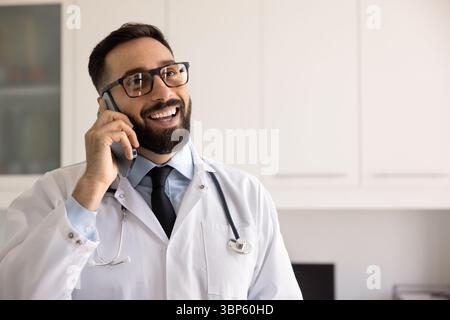 Glücklicher gutaussehender männlicher hispanischer Praktizierender, der auf dem Handy spricht Stockfoto