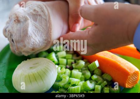 Hände, die ein großes Stück Fleisch über einem Teller mit geschnittenem ​​vegetables halten, einschließlich Selleriehalmen, Zwiebeln und Karotten. Stockfoto