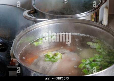 Ein Edelstahltopf mit Glasdeckel wird auf den Herd gestellt, wo die Brühe mit Fleisch kocht Stockfoto
