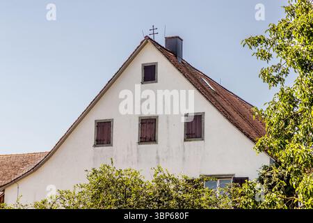 Altes Bauernhaus auf der Klosterinsel Reichenau. Ein Doppelkreuz steht auf dem Giebel, ein Zeichen dafür, dass es sich um ein Lehnsgut handelt, das zum Kloster gehört. Das Doppelkreuz ist auch ein Symbol des göttlichen Schutzes gegen Stürme, Blitzeinschläge und Feuer. Dieses Bild zeigt ein traditionelles Haus mit benachbarten Gärten und Feldern in der Hochwartstraße auf der Insel Reichenau in Baden-Württemberg. Das Doppelkreuz auf dem Dach weist auf seinen ursprünglichen Status als Feudalgut hin. Sie vermittelt einen Eindruck vom ländlichen Leben und dem landwirtschaftlichen Charakter des UNESCO-Weltkulturerbes. Hochwartstraß Stockfoto