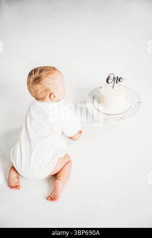 Baby krabbelt in der Nähe der ersten Geburtstagskuche auf weißem Boden Hintergrund. Stockfoto