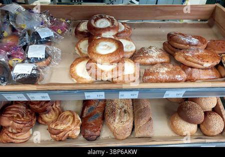 Warme Brötchen und süßes Gebäck werden auf Holzregalen in einer Bäckerei präsentiert. Verschiedene Backwaren erfreuen sich mit köstlichen Aromen und Appetiali Stockfoto