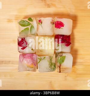 Kreative Anordnung bunter Blumen in Eiswürfeln auf hölzernem Hintergrund. Sonniges Tageskonzept. Stockfoto