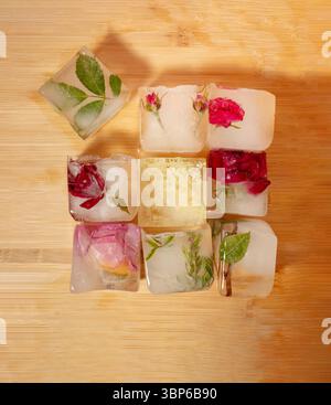 Kreative Anordnung bunter Blumen in Eiswürfeln auf hölzernem Hintergrund. Sonniges Tageskonzept. Stockfoto