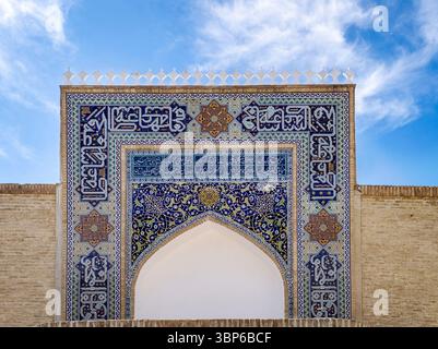 Ein atemberaubendes architektonisches Detail mit komplexen blauen Fliesen und arabischer Kalligraphie auf einem großen Bogengang vor einem hellblauen Himmel. Stockfoto