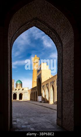 Ein atemberaubender Blick durch einen Bogengang, der einen historischen Komplex mit einem hohen Minarett und Kuppelbauten unter einem blauen Himmel zeigt. Das komplizierte Mauerwerk Stockfoto