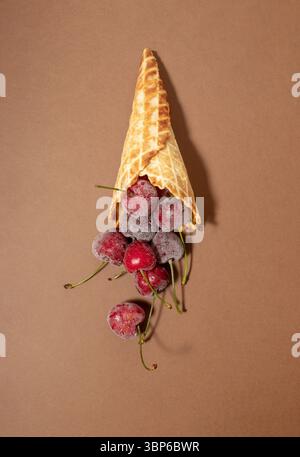 Gefrorene Kirschen in Eiskegel, auf braunem Hintergrund. Stillleben, Flat Lay Stockfoto