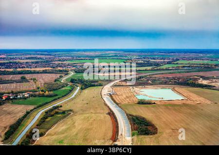 Straße im Bau in Herbstfeldern in der Nähe von Bratislava in der Slowakei, Draufsicht. Aus der Vogelperspektive auf landschaftlich reizvolles Ackerland, gewundenen Kanal, Baustelleninfrastruktur Stockfoto