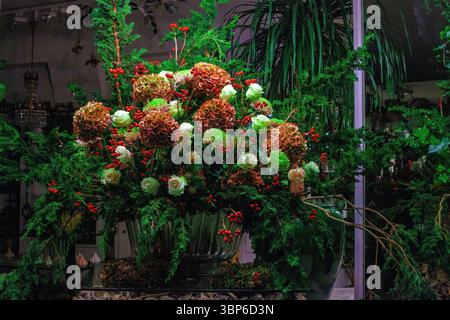 Großer Blumenstrauß in großer Vase im Blumenladen. Festliche atemberaubende Anordnung aus roten Hortensien, weißen Rosen und Zypressen-immergrünen Zweigen, schmücken Stockfoto
