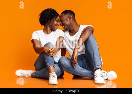 Emotionale schwarze Liebhaber kuscheln auf orangefarbenem Hintergrund Stockfoto