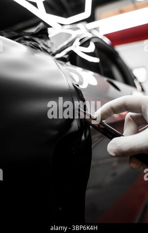 Vinyl-Verpackung Für Autos Mit Vollpaneel. Die großformatige Vinylfolie verwandelt das Außenmaterial des Fahrzeugs mit mattschwarzer Folie. Änderungen an der Anwendung der Autoverpackung Stockfoto