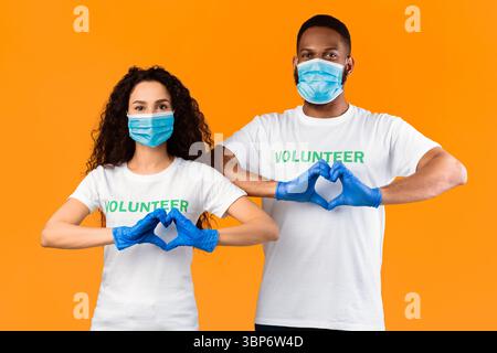 Zwei Freiwillige Gestikulieren Herz-Form Tragen Masken Und Handschuhe, Gelber Hintergrund Stockfoto