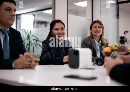 Ein gemeinschaftliches Geschäftstreffen mit lächelnden Fachleuten versammelte sich an einem Tisch in einem modernen Büro und diskutierte Ideen mit Enthusiasmus und Teamwork. Stockfoto