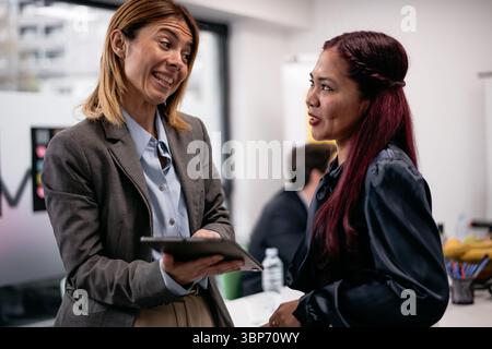 Zwei professionelle Frauen führen eine Diskussion und schaffen eine kollaborative und freundliche Atmosphäre in einer modernen Arbeitsplatzszene. Ihre Interaktion vermittelt Stockfoto