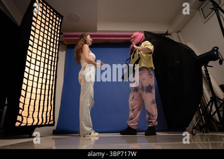 Professionelle Studioumgebung mit einem Motiv und einem Fotografen, der bei einer Porträtfotosession mit Studiobeleuchtung und einem farbenfrohen bac arbeitet Stockfoto