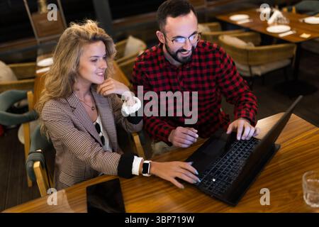 Zwei Kollegen arbeiten in einem Café an einem Laptop zusammen und demonstrieren Teamarbeit, Produktivität und eine entspannte Arbeitsatmosphäre. Sie diskutieren Ideen und Stockfoto
