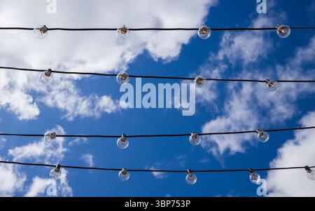 Glühbirnen auf der Straße bei Tageslicht. Eine Girlande elektrische Drähte mit Lampe gegen blauen Himmel. Altmodische Dekoration mit Himmelshintergrund Stockfoto