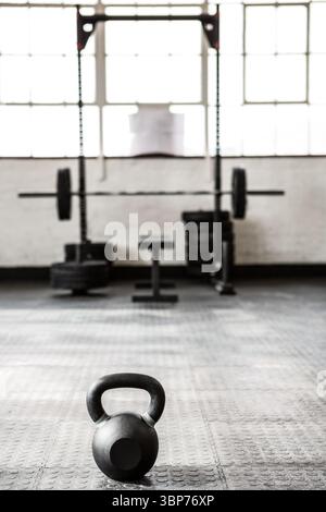 Die schwarze Kettlebell sitzt auf Gummiboden in einem flachen Design-Fitnessstudio mit Hockgestell und Langhantel Stockfoto