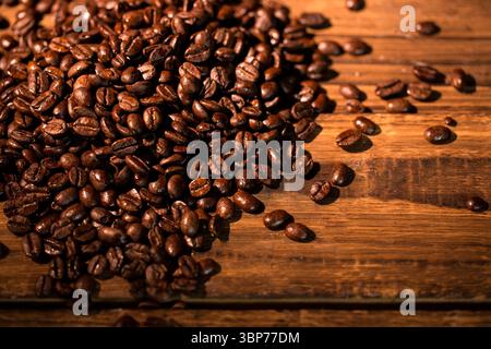 Die flache Abbildung zeigt einen Haufen gerösteter Kaffeebohnen, die auf Holzoberfläche mit Holzmaserung glänzen Stockfoto