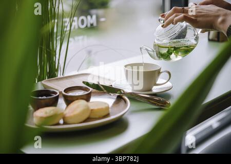 Essen, Eine Hand, die Tee aus einer Teekanne aus Glas gießt Stockfoto